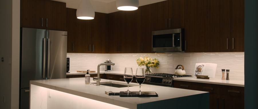 contemporary kitchen with dark wooden cabinets and a white countertop with LED light fixtures hanging from above